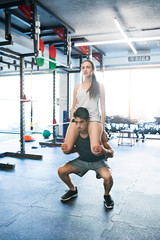 Obraz premium Man carrying woman on his shoulders, doing squats.