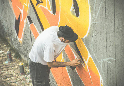 Graffiti artist covering his face while painting with aerosol color spray on the wall