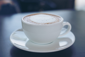 Closeup image of a white cup of hot coffee on vintage wooden table