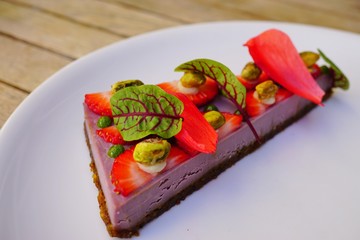 Slice of vegan strawberry cheesecake with a pistachio nut crust and blood sorrel leaves