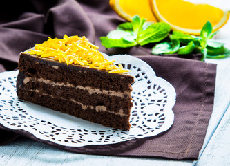 A piece of chocolate cake on a dark napkin with orange slices and mint