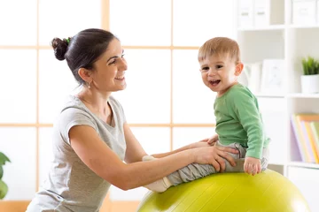 Fotobehang Happy mother with baby son doing gymnastics on the big fitness ball in the gym. © Oksana Kuzmina