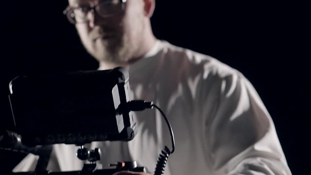 Smooth movement of the camera in the protective cage installed on the stabilizer in the hands of the operator with the glasses focusing on the screen recorder.