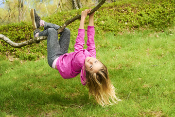 Child blond girl climbing a tree in a park outdoor. Upside down