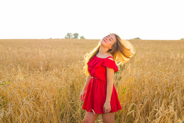 Gorgeous Romantic Girl Outdoors. Beautiful Model in Short Red Dress in Field. Long Hair Blowing in the Wind. Backlit, Warm Color Tones.