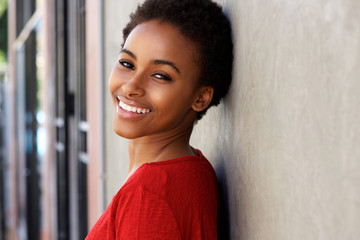 happy young black woman leaning against wall and smiling