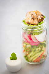 Vegetable mix and chicken slices  in a glass jar yogurt sauce  on wooden table. Clean eating. Healthy denner.