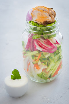 Vegetable mix and chicken slices  in a glass jar yogurt sauce  on wooden table. Clean eating. Healthy denner.
