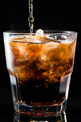 stream of cola is poured into a glass with ice