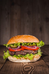 Fresh burger in bun with sesame with lettuce, tomato, beef and onion on wooden table.