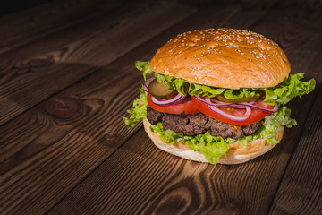Fresh burger in bun with sesame with lettuce, tomato, beef and onion on wooden table.