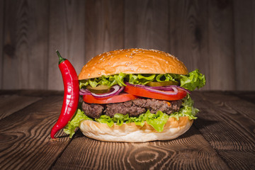 Fresh burger in bun with sesame with lettuce, tomato, beef and onion on wooden table.