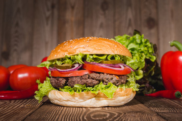 Fresh burger in bun with sesame with lettuce, tomato, beef and onion on wooden table.