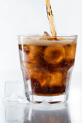 stream of cola is poured into a glass with ice