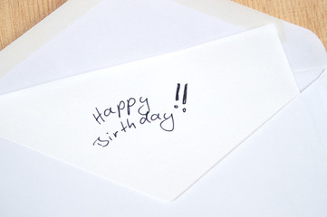 Happy Birthday, handwritten letter in white envelope, wooden background