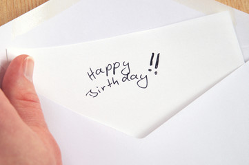 Happy Birthday, hand holding handwritten letter in white envelope, wooden background