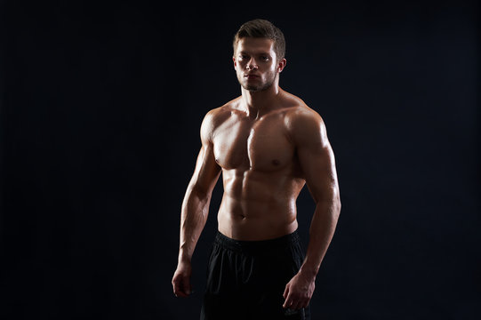 Handsome strong athletic young man fitness model showing off his abs six-pack posing shirtless on black background copyspace athletics body torso masculinity sexy sportsman sport fitness bodybuilder.
