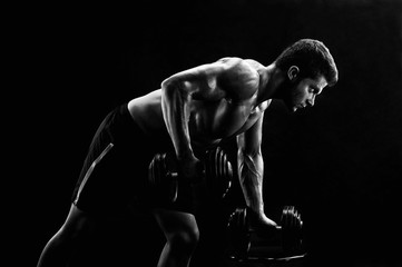 Obraz na płótnie Canvas Monochrome low key lighting shot of a strong fit and toned young man exercising with dumbbells doing triceps workout gym motivation masculinity active athletics physique confidence focusing.
