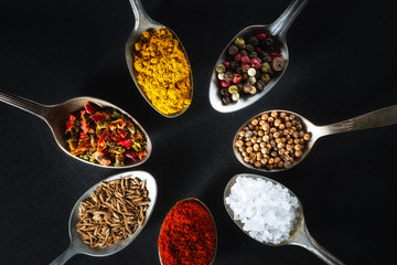 spoons with salt and spices on black chalkboard