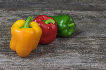The group of three colored peppers standing behind each other on an old wooden table