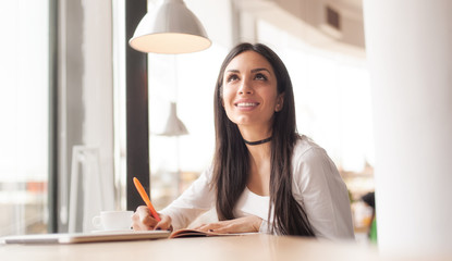 Young woman writing in her notebook and drinking morning coffee