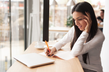 Young woman writing in her notebook and drinking morning coffee