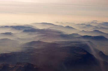 Fototapeta na wymiar Mountain shop from the plane in Alps at sunset, cloudy, misty mountains