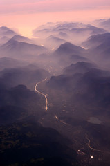 A view from above to Alps at sunset, misty mountains, pink fog clouds, sun reflection in the river,...