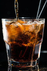stream of cola is poured into a glass with ice