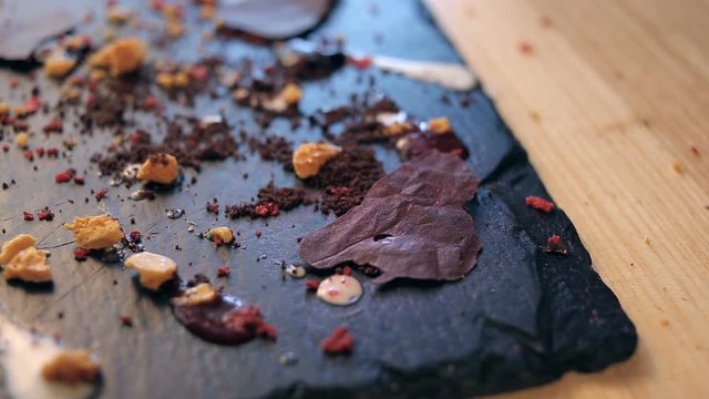dolly rotation shot of blowing a sugar dust on a chocolate dessert. Dessert decorated with a cream, honey crumbs and picies of chocolate. Making in a restaurant.
