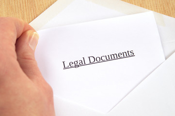 Legal Documents printed on white paper and envelope, hand holding it, wooden background