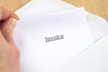 Invoice printed on white paper and envelope, hand holding it, wooden background