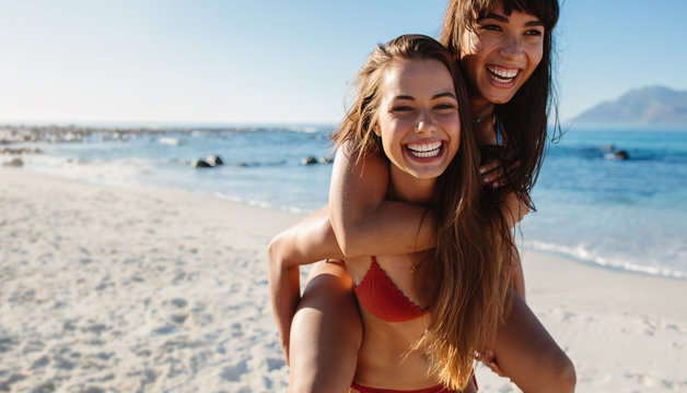 Beach vacation, young woman carrying her friend on back.