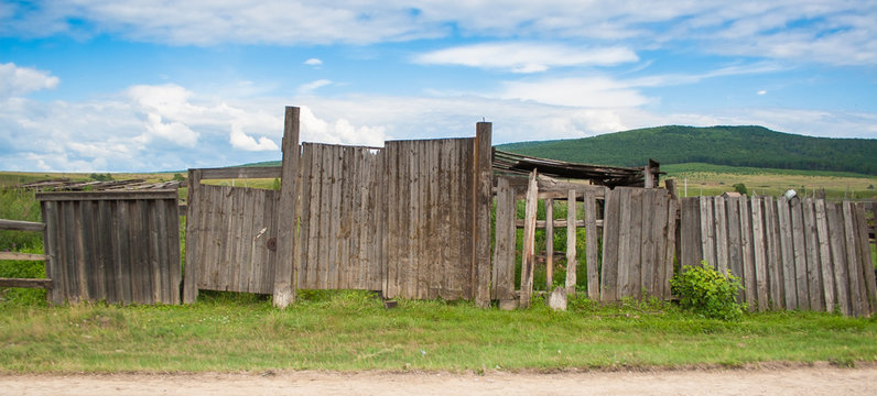 Old fence in rural areas. Green grass near an abandoned fence on the background of blue sky.