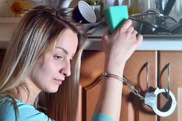 Sad and tired girl handcuffed to a kitchen counter with a lot of unwashed dishes