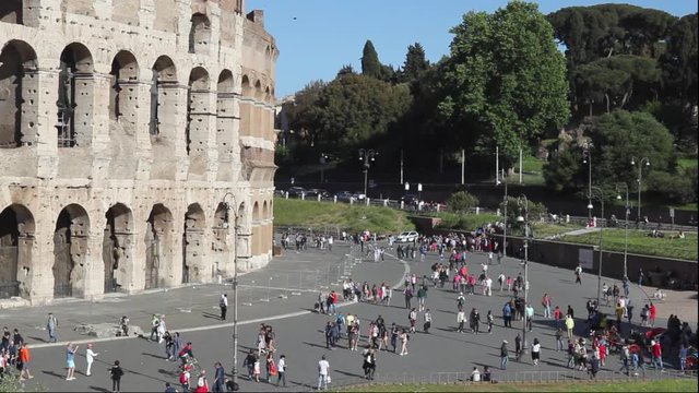 Colosseum Square, a crowd of tourists and citizens stroll through the pedestrian area in front of the monument.