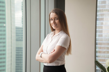 Confident businesswoman enjoys success. Happy woman standing in office with arms crossed, looking at camera. Smiling ambitious female entrepreneur thinking about business, feeling positive. Portrait