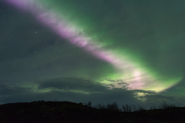 The Aurora and clouds in the sky above the hills .