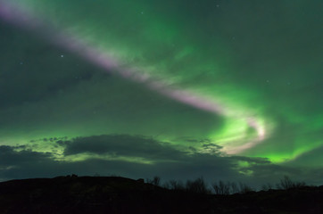 The Aurora and clouds in the sky above the hills .