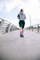 Beautiful young woman running on bridge during a training session in spring afternoon