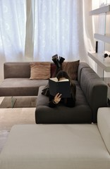 Girl reading a book at home on the sofa. Italy