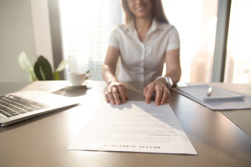 Smiling realtor sitting at the table with rental agreement. Close up photo of real estate rent contract. Businesswoman reading conditions of rent at workplace. Satisfied client ready to strike a deal