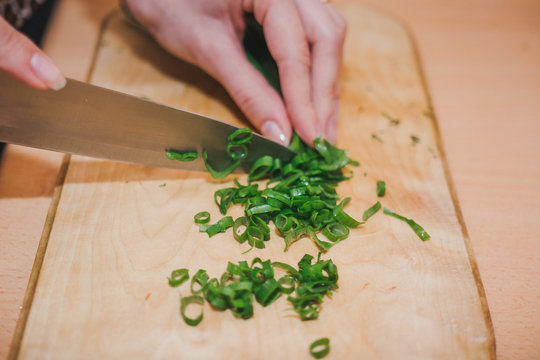 To cut green onions. The girl cuts green onions on a wooden board.