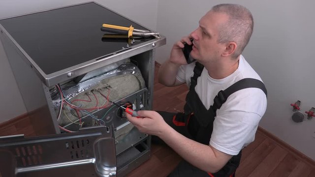 Electrician checking electric cooker and talking on phone