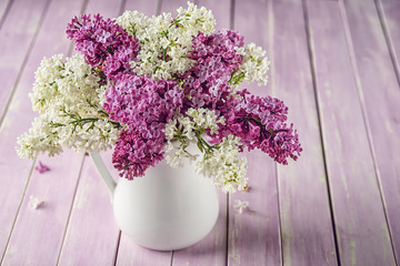 still life with purple and white lilac in white vase on pink table, spring blooming plant with petals