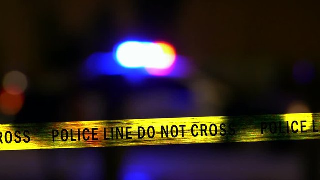 Crime scene tape with defocused flashing police car siren in background