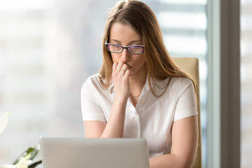 Young woman attentively looking on laptop screen at office. Businesswoman mulling decision of problem. Female entrepreneur ponders an answer on e-mail. Thoughtful office worker doubts about results - obrazy, fototapety, plakaty