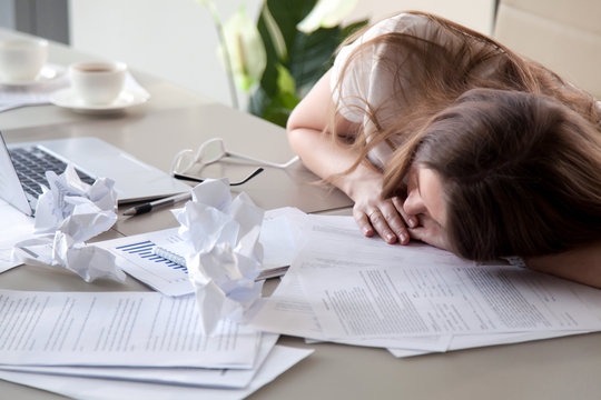 Tired woman sleeping at workplace covered crumpled papers. Overworked female entrepreneur give up after hard day and dozing at desk. Stressed businesswoman lying on table with documents under her head