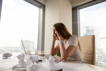 Stressed businesswoman screaming at  desk covered crumpled paper. Female entrepreneur feeling...
