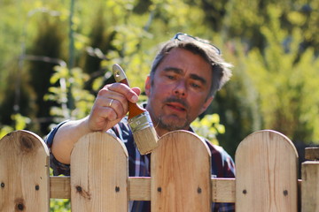 Mann im Garten beim Streichen des Zaunes